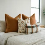 Marenca burnt orange cushions on bed with floral and plaid patterns in warm tones.