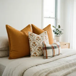 Marenca ginger cushions arranged on bed with floral and plaid patterns in warm tones.