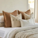Marenca tan cushions styled on bed with layered neutrals and textured lumbar cushion.
