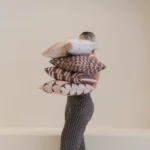 Person holding stacked Solterra cushions featuring brown and blush geometric designs.
