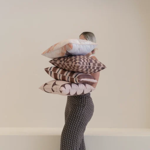 Person holding stacked Solterra cushions featuring brown and blush geometric designs.