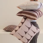 Person holding stacked Solterra cushions in warm brown striped and abstract patterns.