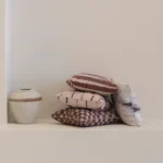 Solterra cushions stacked on shelf beside ceramic vase in neutral interior.