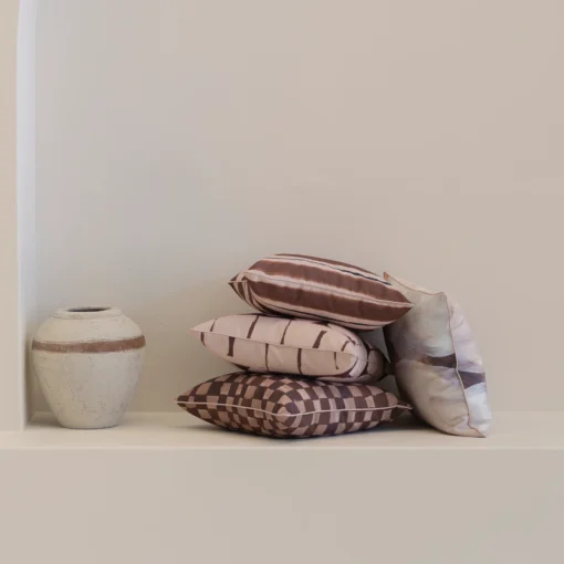 Solterra cushions stacked on shelf beside ceramic vase in neutral interior.