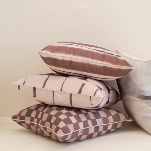 Close-up of stacked Solterra cushions with brown check, stripe and abstract designs.