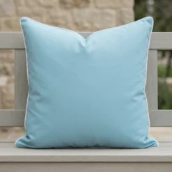 Tropica aqua cushion with white piping on outdoor wooden bench.