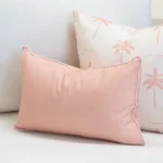Tropica pink cushion with white piping beside palm print cushion on sofa.