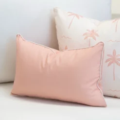 Tropica pink cushion with white piping beside palm print cushion on sofa.