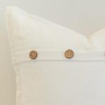 Close-up of white linen cushion with natural wooden button closure and clean, crisp finish.