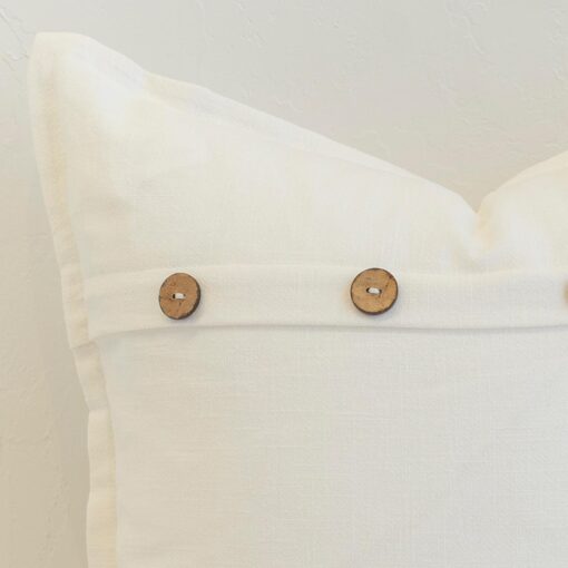 Close-up of white linen cushion with natural wooden button closure and clean, crisp finish.
