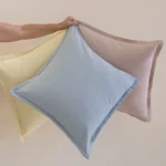 Hand holding pastel linen cushions in yellow, blue and soft pink tones.