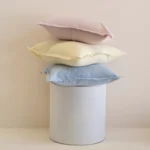 Pastel linen cushions stacked on white pedestal in soft pink, yellow and blue tones.