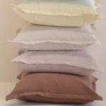 Stack of linen cushions in pastel shades including cream, lilac and rust.