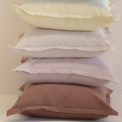 Stack of linen cushions in pastel shades including cream, lilac and rust.
