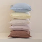 Stack of pastel linen cushions in blue, yellow, cream, lilac and rust tones.