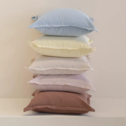 Stack of pastel linen cushions in blue, yellow, cream, lilac and rust tones.