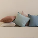 Stacked linen cushions in soft pastel tones including blue, yellow, blush and rust.