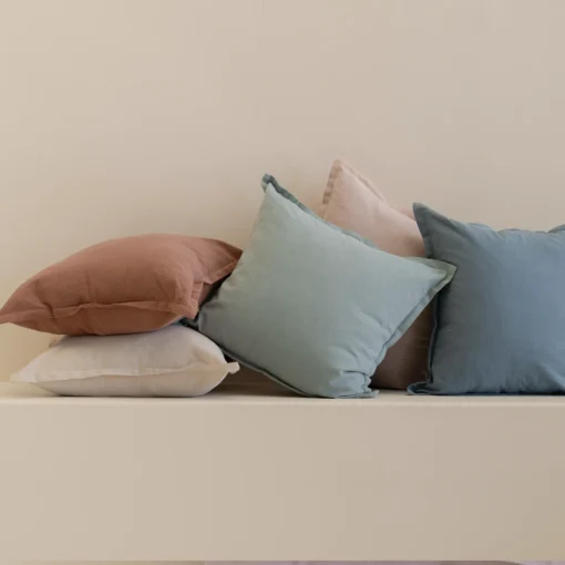 Stacked linen cushions in soft pastel tones including blue, yellow, blush and rust.